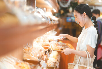 Happy smiling customer asian woman choosing whole grain bread at bakery shop