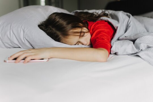 Pretty teenage girl lying under covers on bed. Getting up early in the morning, the overslept school. The alarm is waking herm up. Generation alpha and new day concept. Part of a series