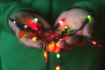 Close-up of a Man in a green jumper holding a handful of illuminated multi coloured christmas string lights