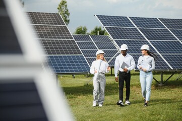 Group of multi ethnic people and safety helmets staring at solar farm.