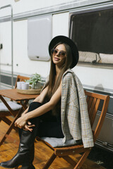 Camper life, a woman sitting on chairs and picnic table with her camper housing behind, in the...