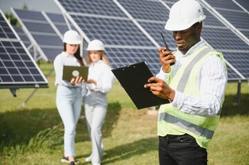 Group of multi ethnic people and safety helmets staring at solar farm.