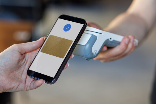 A customer uses a smartphone to make a contactless payment at a grocery store checkout, demonstrating modern NFC technology for convenient transactions