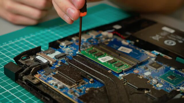Son unscrewing bolts while assisting father in laptop cooling system disassembly. Boy using screwdriver for laptop repair, collaborating with male mentor. Kid removing screws for computer maintenance