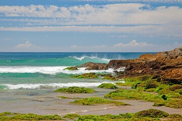 Rocky shoreline on the Golden Coast, Australia, with moss-covered rocks and crashing ocean waves