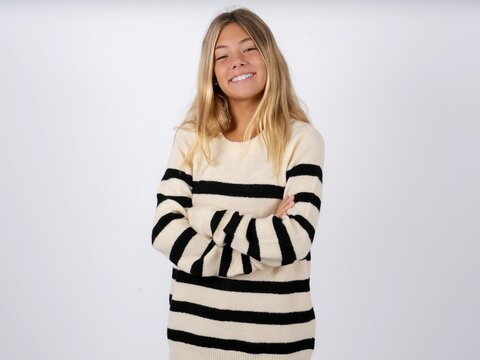 Beautiful teen girl wearing striped sweater happy face smiling with crossed arms looking at the camera. Positive person.