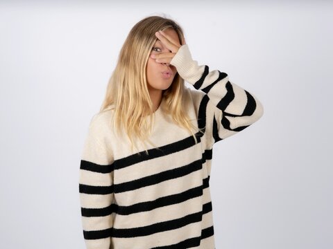 Beautiful teen girl wearing striped sweater peeking in shock covering face and eyes with hand, looking through fingers with embarrassed expression.