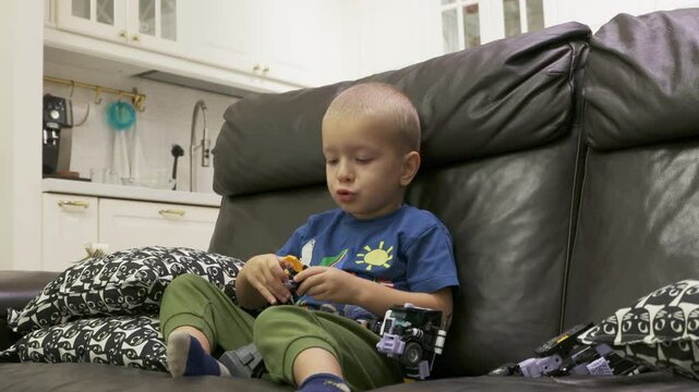 Child playing with new toy sitting on sofa at home. Concentrated face of little boy holding transformer robot toy. Three year old child examining new toy comments on his actions.