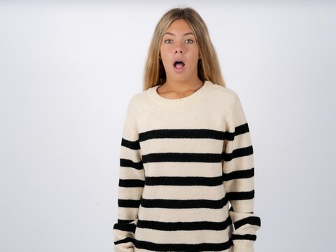 Oh my God. Surprised Beautiful teen girl wearing striped sweater stares at camera with shocked expression exclaims with unexpectedness,