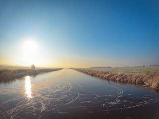 A completely frozen lake in the morning at sunrise. Typical Dutch rural landscape in winter season