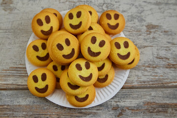 Smiley face shortbread cookies are stacked on a white plate on a wooden table in close-up, top...