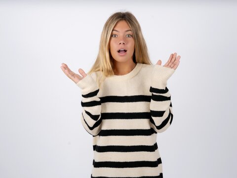 Surprised terrified Beautiful teen girl wearing striped sweater Gestures with uncertainty, stares at camera, puzzled as doesn't know answer on tricky question, People, body language, emotions concept