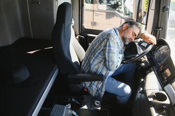 Tired of work. Sitting in the cabin. Young truck driver is with his vehicle at daytime
