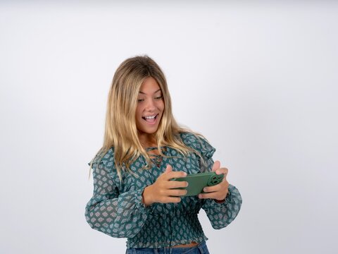 Portrait of an excited Beautiful teen girl wearing green fashion T-shirt playing games on mobile phone.