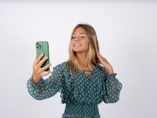 Beautiful teen girl wearing green fashion T-shirt smiling and taking a selfie ready to post it on...