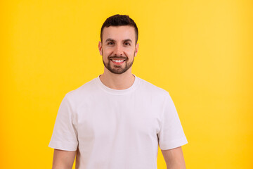Smiling man in a white shirt posing against a vibrant yellow background.