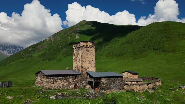 Aerial Drone Footage Captures The Stunning Lamaria Church In Ushguli, Georgia, Surrounded By Majestic Snow-Capped Mountains On A Cloudy Summer Day, Evoking A Sense Of History And Beauty.