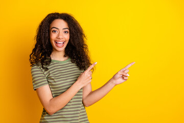 Fototapeta premium Photo of overjoyed girl with wavy hairstyle dressed striped t-shirt directing at discount empty space isolated on yellow color background