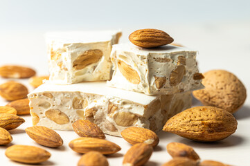 Pieces of hard nougat with almonds, with almonds next to it, on a light wooden surface. 
