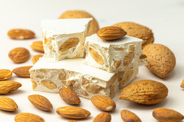 Pieces of hard nougat with almonds, with almonds next to it, on a light wooden surface. 
