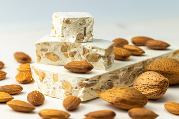 Pieces of hard nougat with almonds, with almonds next to it, on a light wooden surface. 
