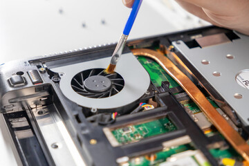 Obraz premium cleaning laptop cooling fan using a brush during maintenance, visible motherboard and copper heat pipes
