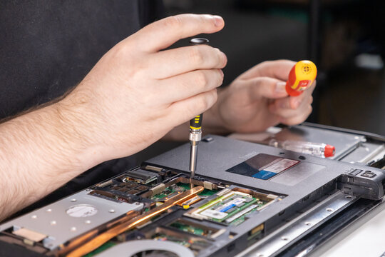 tightening screws on a laptop during disassembly or reassembly, close-up of a technician using precision tools for repair or maintenance work