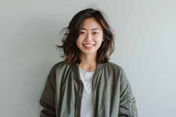 Fototapeta premium Portrait of a smiling asian woman in her 20s wearing a trendy bomber jacket in minimalist or empty room background