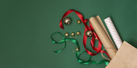 Creative Christmas composition of ribbons and paper and decorations from a brown paper bag on green background space for text. Concept: season of packing and buying with gift for the winter holidays