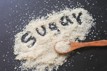 spoonful of sugar. sugar on black background. the word 'sugar' is spilled with sugar