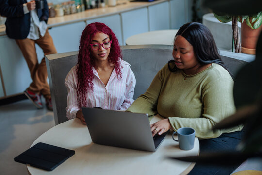 Two businesswomen collaborating on laptop in modern office cafe - Powered by Adobe