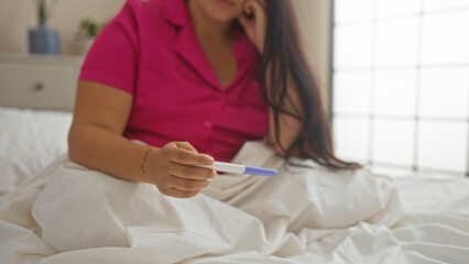 Young woman in a bedroom holding a pregnancy test in hand while sitting on a bed © Krakenimages.com