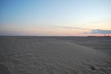 A serene desert landscape at dusk, featuring soft sand dunes under a pastel-colored sky. The gentle hues of the horizon and the undisturbed terrain create a tranquil and minimalist scene.