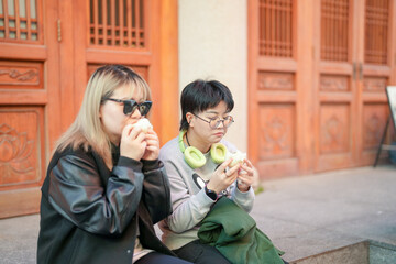 Two Chinese women in their 30s eating steamed buns in front of historical building in Jing'an District, Shanghai, China