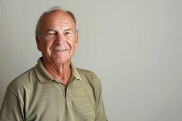 Portrait of a glad caucasian man in his 70s wearing a sporty polo shirt over blank studio backdrop