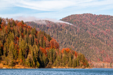 Beautiful view of the foothills of the Alps on an autumn evening. Water and yellow-red trees	
