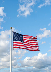 American flag waving under blue sky with fluffy white clouds