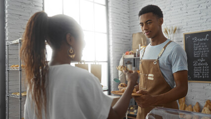 Obraz premium Woman customer interacting with man baker in a cozy bakery interior, showcasing freshly baked goods on a sunny day indoors.
