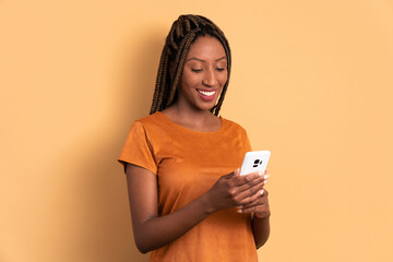 cheerful black woman looking at mobile cell phone screen in beige colors. app, social media,...