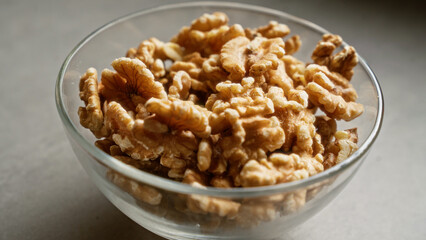 Close-up of a glass bowl filled with delicious, fresh walnuts on a smooth, grey surface in natural...