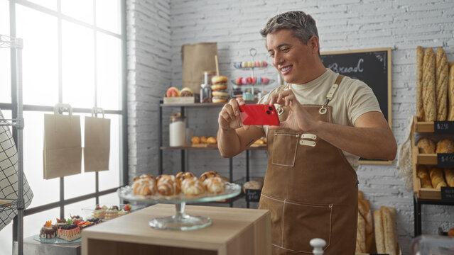 Young man capturing photos of pastries with his smartphone in a cozy bakery with a variety of baked goods on display