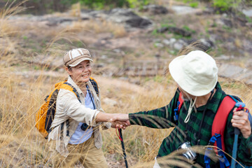 bonding asian senior woman holding hand her husband while hiking in the forest,active senior couple with backpack and trekking poles enjoy exploring in nature