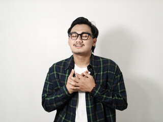 Portrait of smiling pleasant Young Asian man in plaid shirt looking camera and holding hands on his chest, heart isolated on white background