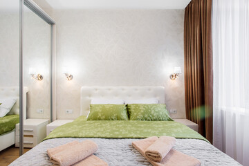 A well-appointed small modern bedroom with a cozy design, featuring a queen-sized bed, bedside tables. A large window with curtains allowing soft daylight.