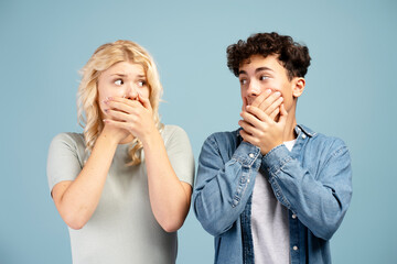 Scared, young boyfriend and girlfriend covering mouth with hands, looking each other