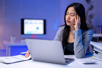 A woman is sitting at a desk with a laptop and a stack of papers