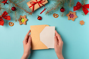 Envelope in female hands with a blank card on a blue background. Christmas concept. Flat lay, top view