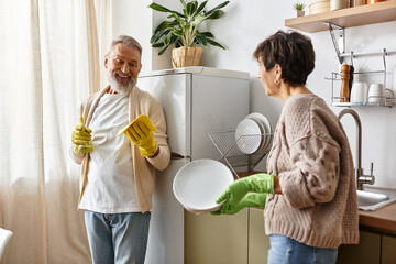 A cheerful mature couple enjoys washing dishes while sharing laughter in their warm kitchen