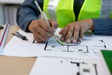A man is holding a model of a house. The house is a small, two-story home with a slanted roof. The man is wearing a safety vest, which suggests that he is working on a construction site