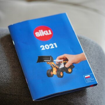 Closeup shot of a closed blue Siku brand brochure from 2021 with toys on a gray couch
